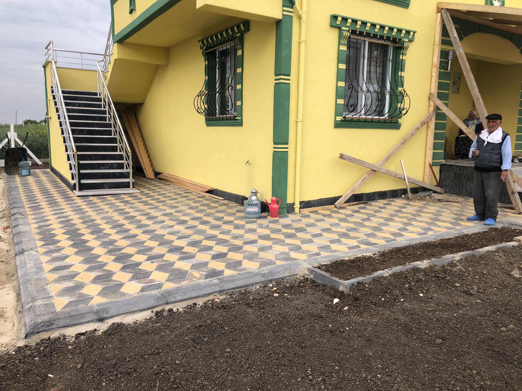 Sarı ev bahçesinde üç boyutlu baklava desenli renkli kilit parke taşı teras döşemesi