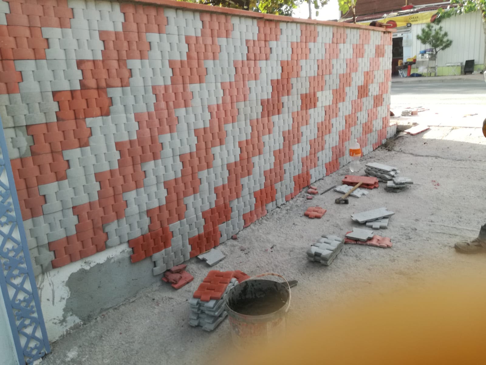 Bahçe duvarına çapraz desenle uygulanan kırmızı ve gri kilit taşı kaplama çalışması