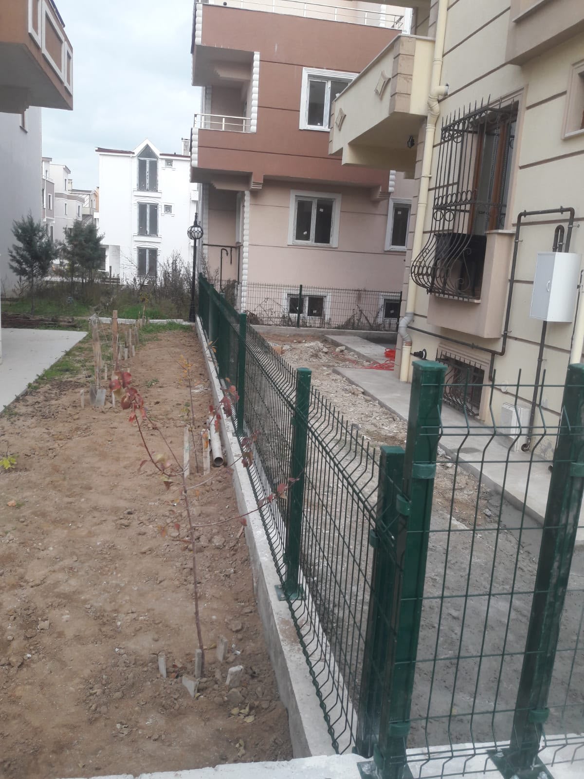 Apartman bahçesi için beton zemin üzerine uygulanan yeşil panel çit montajı